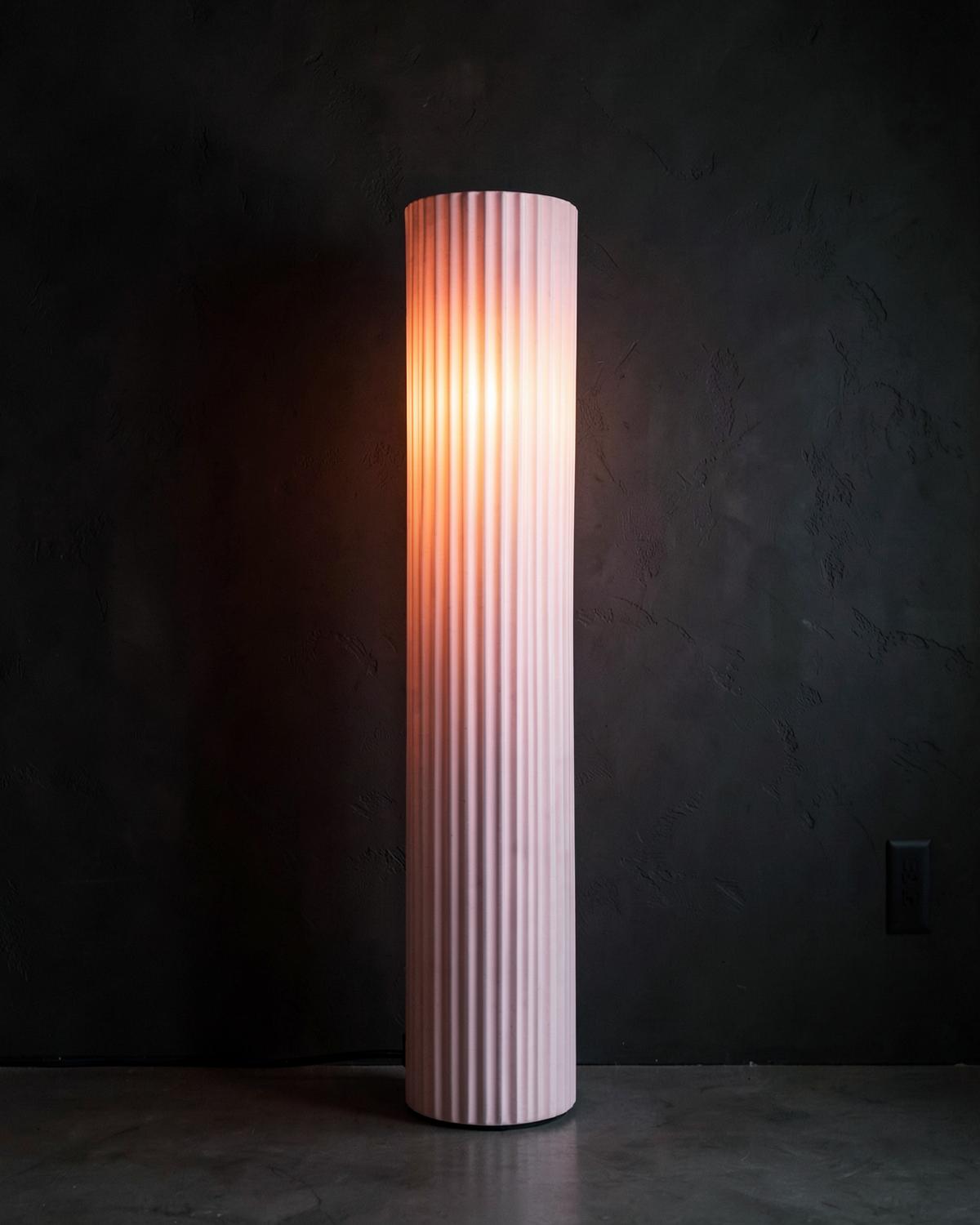 Tall ribbed ceramic column lamp glowing warm pink against a dark wall